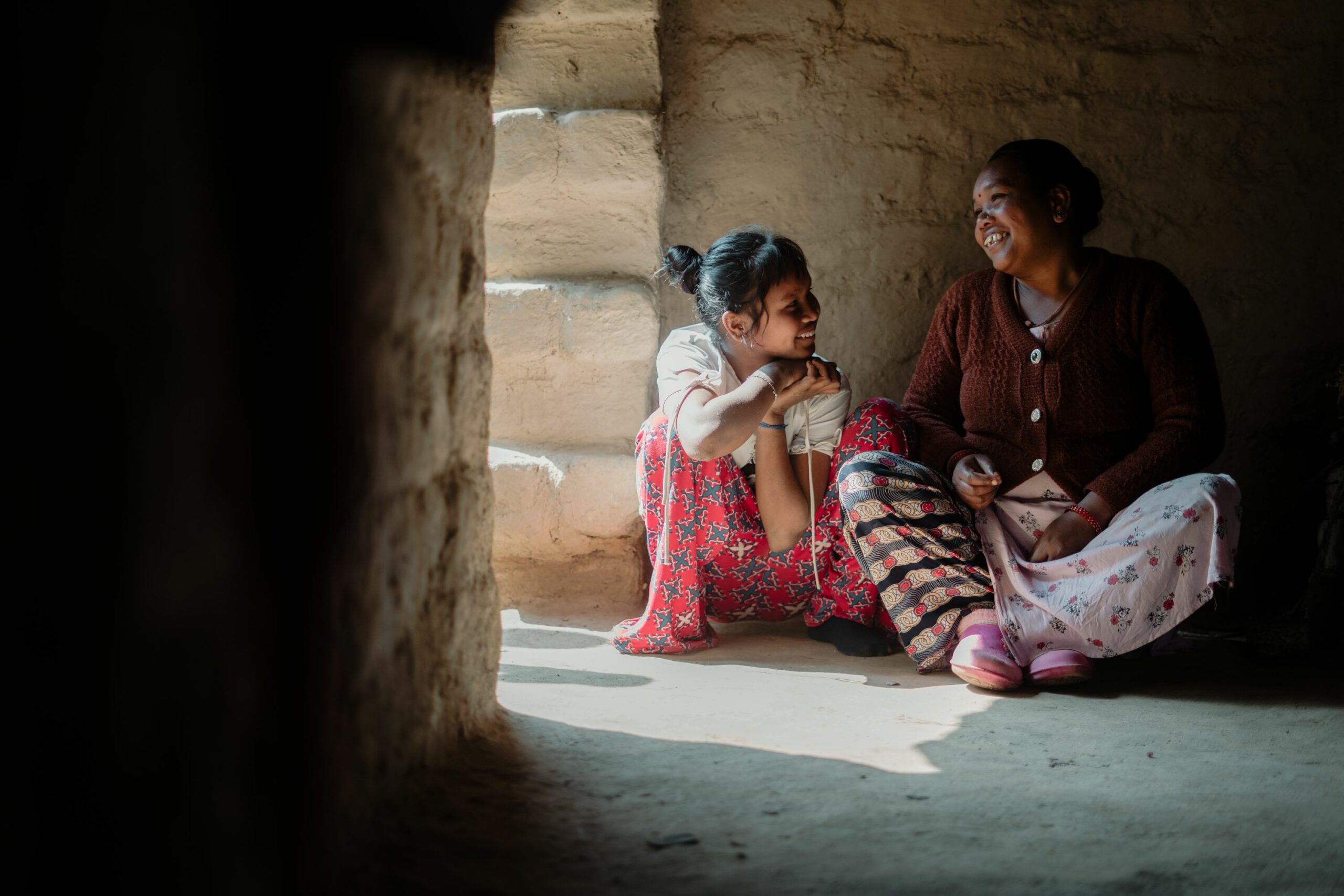 Meisje en haar moeder in Nepal zitten naast elkaar op de grond. 